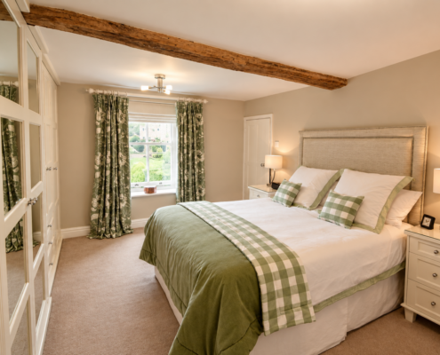 Double bedroom with exposed oak beam, fitted wardrobes and green floral curtains