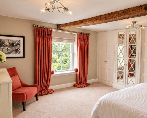 Double bedroom with exposed oak beam, fitted wardrobes and coral armchair